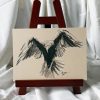 Dessin original à l'encre de Chine et crayon blanc sur chevalet représentant un corbeau de dos en train de s'envoler ©Ysae illustrations