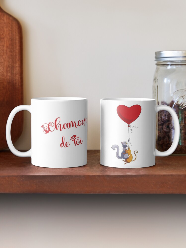 Mug de Saint-Valentin décoré de deux chats mignons, des chats amoureux, qui volent, accrochés à un ballon en forme de cœur. De l'autre côté de la tasse on peut lire "chamoureux de toi" ©Ysae illustrations
