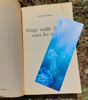 Photo du livre "20 000 lieues sous les mers" avec un mini marque-page illustré représentant des méduses qui danse dans l'eau bleu turquoise de l'océan @ysae illustrations
