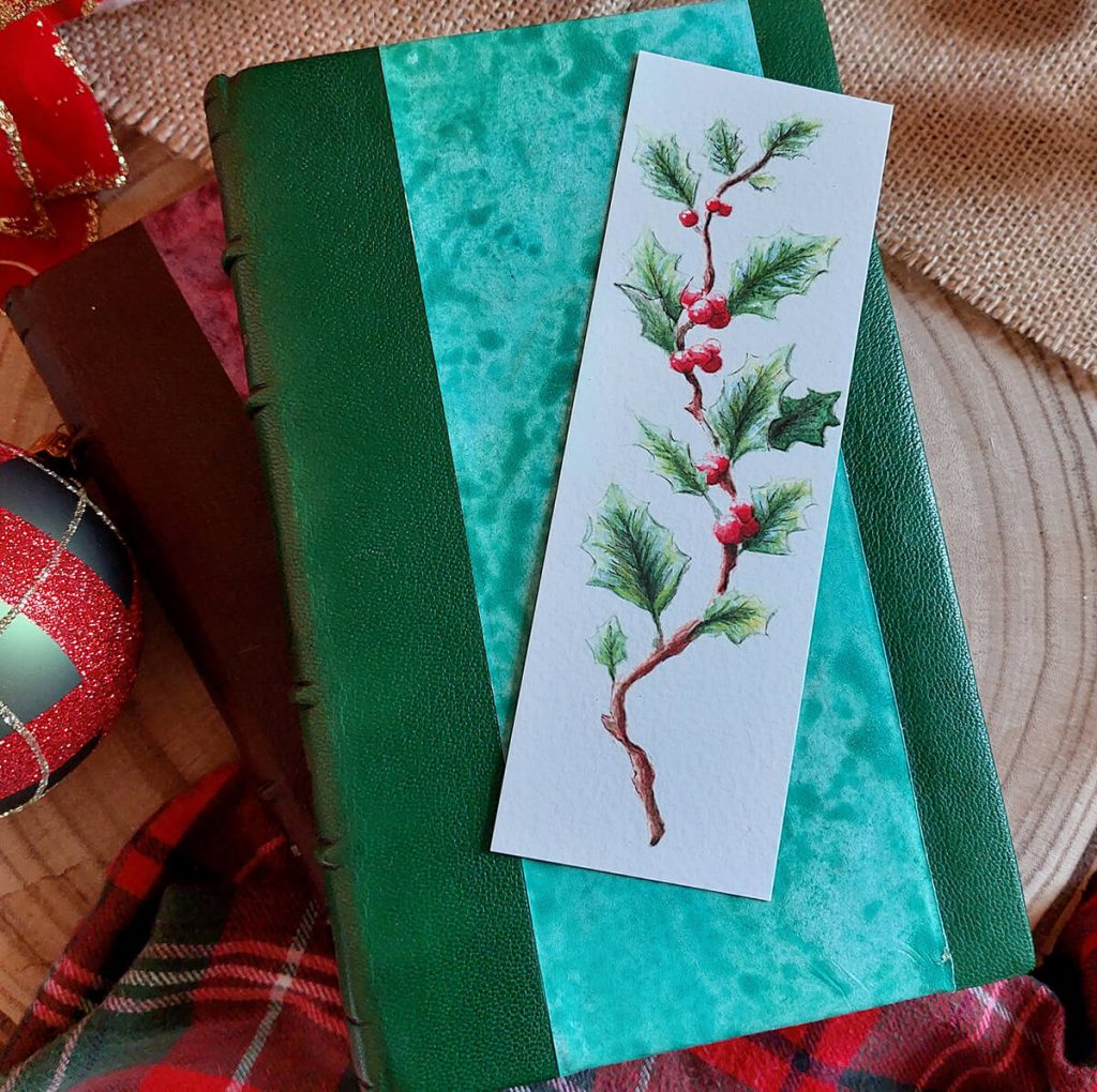 Marque-page illustré d'une branche de houx à l'aquarelle présenté sur un livre relié @Ysae illustrations