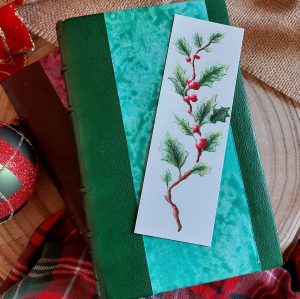 Marque-page illustré d'une branche de houx à l'aquarelle présenté sur un livre relié @Ysae illustrations